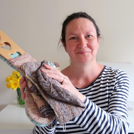 Emma who is the founder of Eldenwood Craft shows her current knitting projects on her podcast. She wears (like she often does) a blue and white striped top.