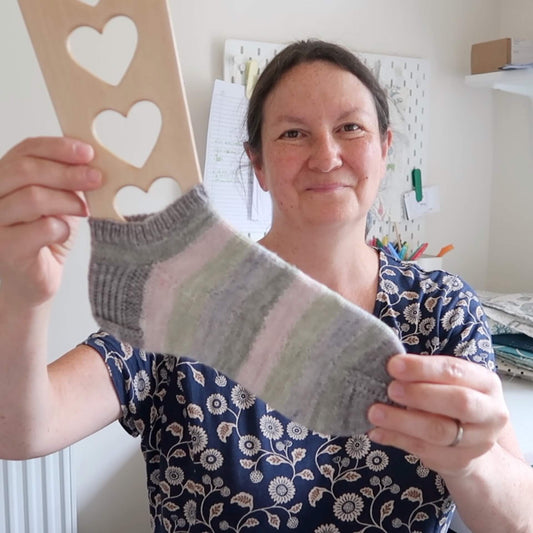 Emma holds a finished hand knit sock to the camera. She is discussing her knitting on her podcast, the Eldenwood Craft Knitting Podcast.