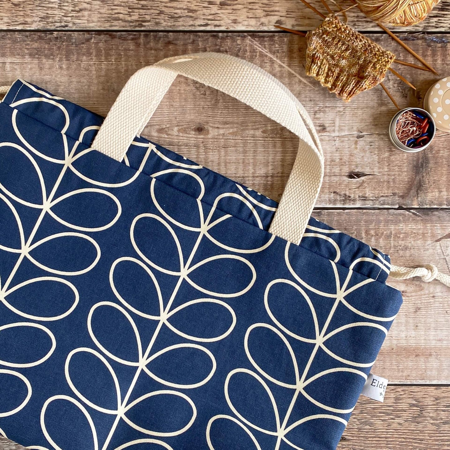 A blue and white knitting project bag lies on a table next to a small knitting project project that has been recently started.