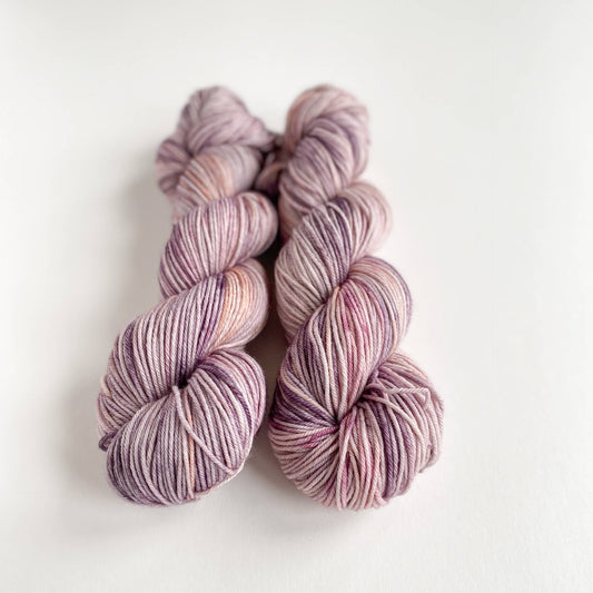 Two skeins of yarn lie on a white background. The yarn has been dyed in pinks and purples.