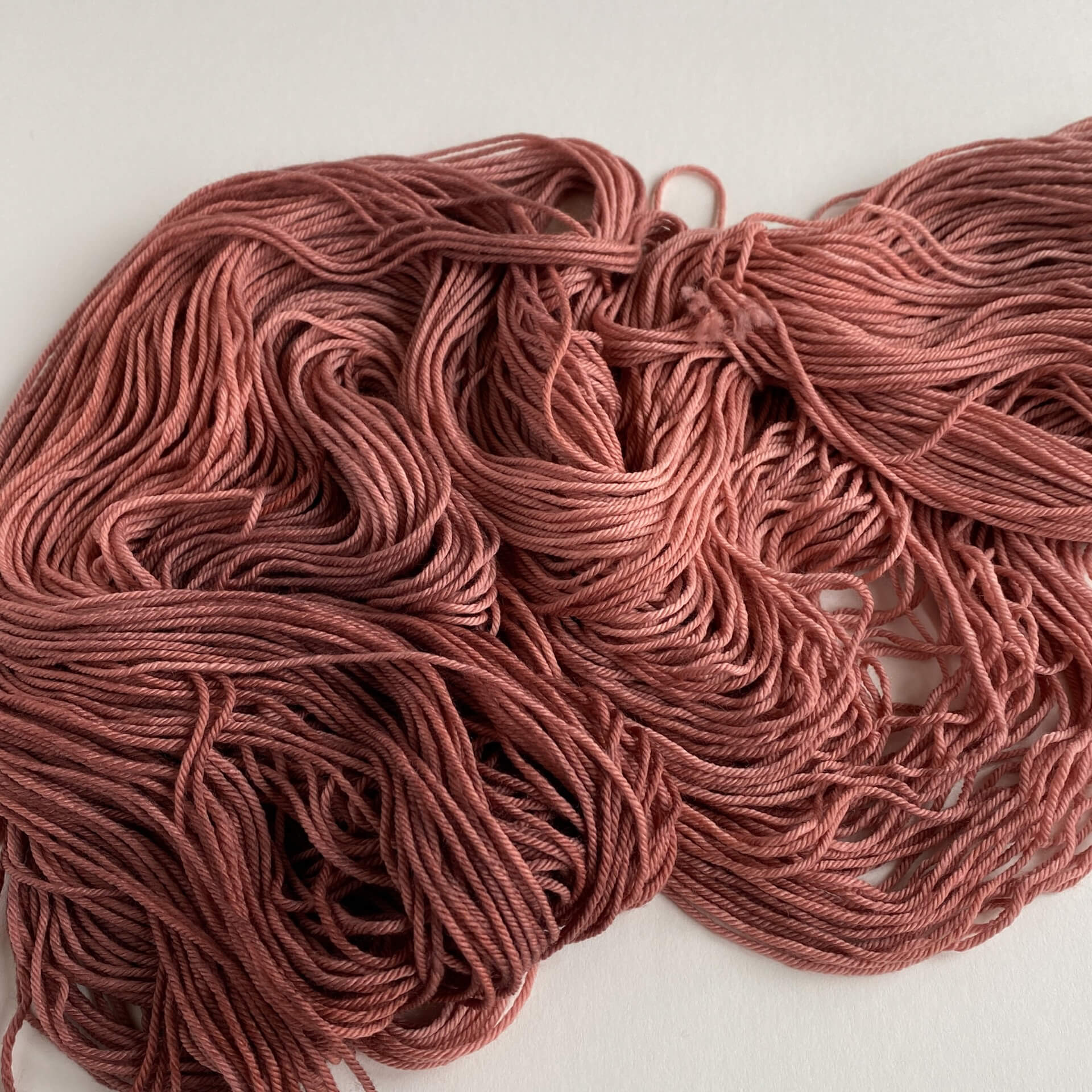 Yarn lies unwound on a white background. It is coloured a dark pink. 