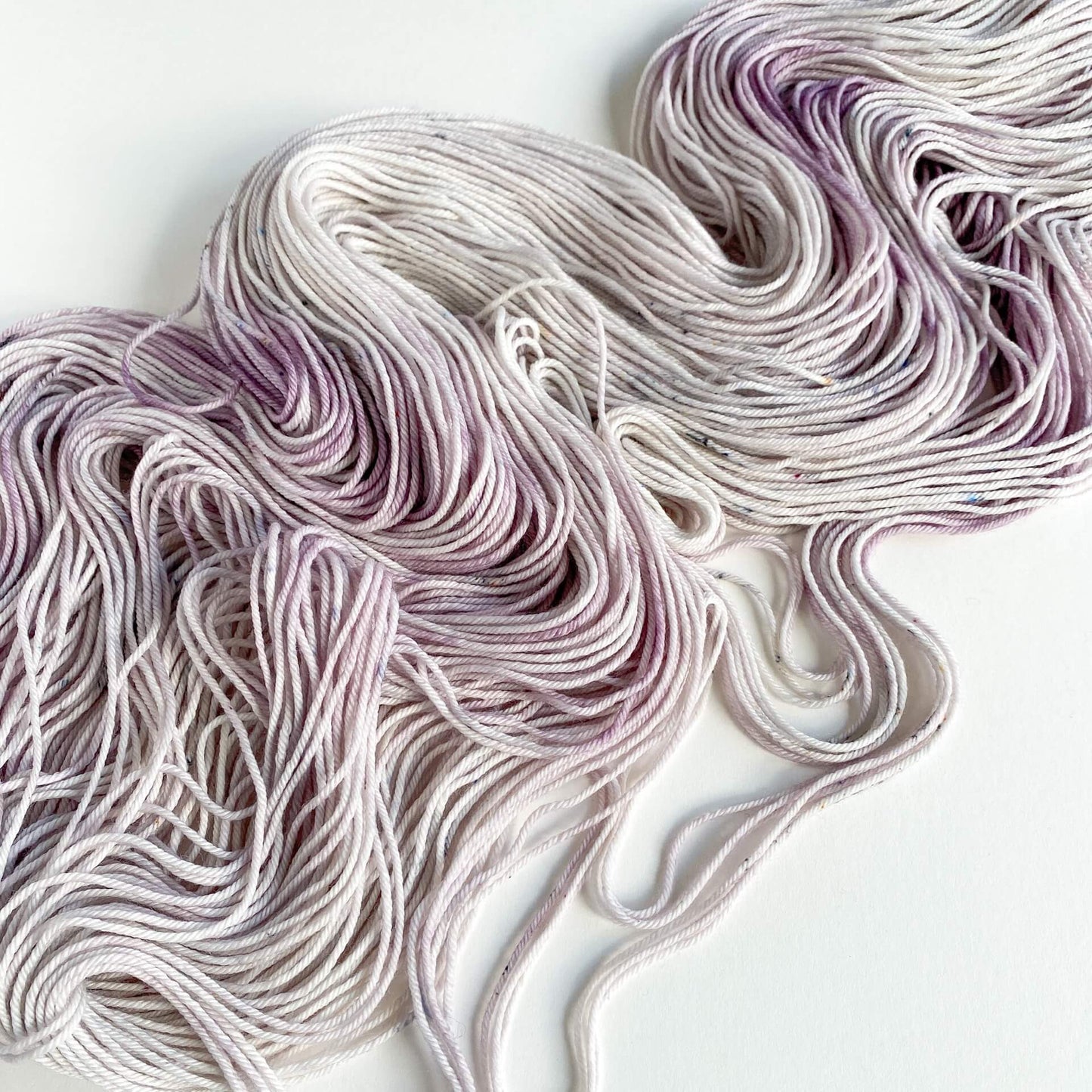 Hand dyed yarn lies scattered across a white table top. The yarn has been dyed with purple and grey dyes.