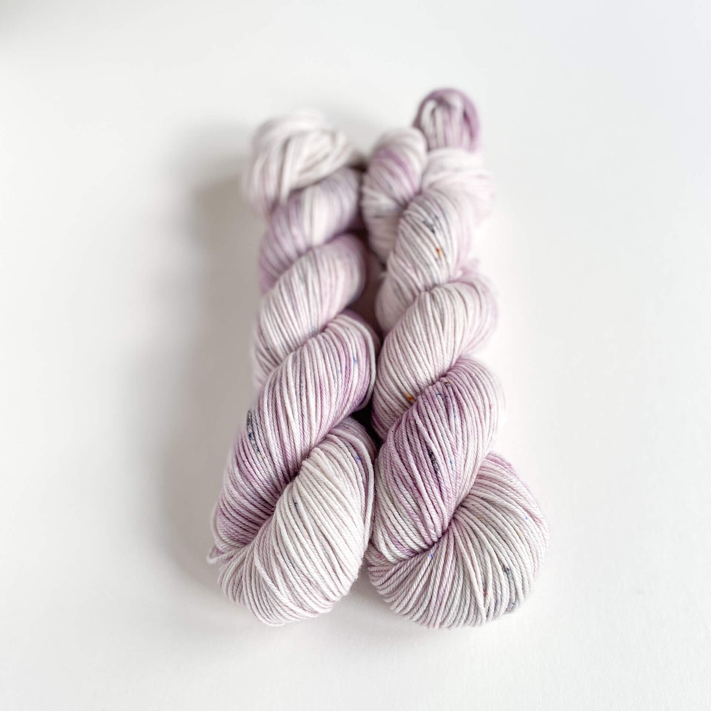 Two skeins of hand dyed yarn on a white table top. The yarn has been dyed with purple and grey dyes.