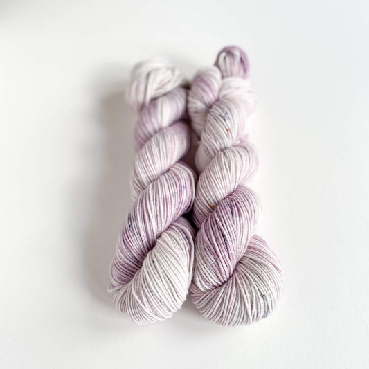 Two skeins of hand dyed yarn on a white table top. The yarn has been dyed with purple and grey dyes.
