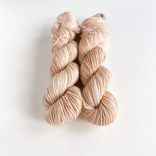 Two skeins of hand dyed yarn on a white table top. The yarn has been dyed with brown and pink dyes.