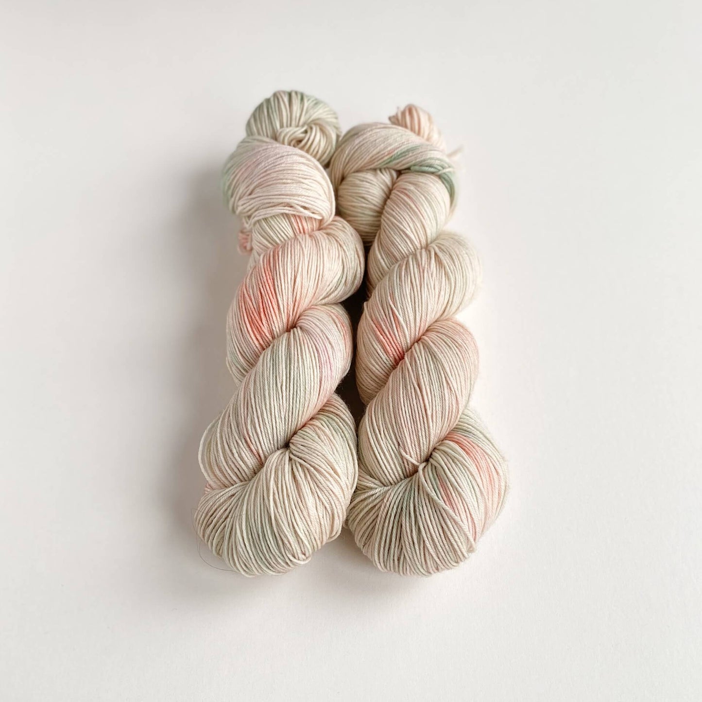 Two skeins of hand dyed yarn on a white table top. The yarn has been dyed with pink, green and grey dyes.