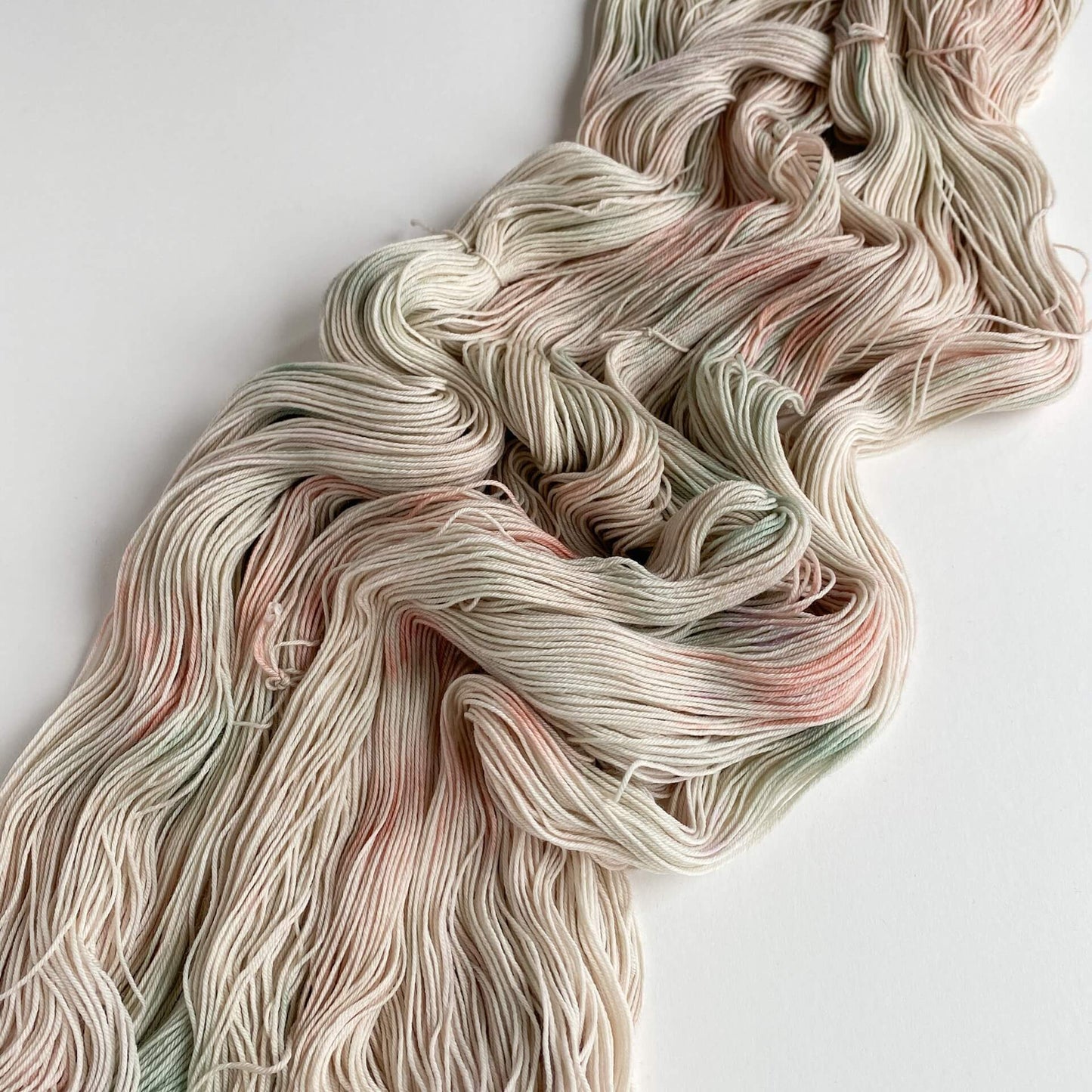 A pink, green and grey skein of yarn has been unfurled from its skein and tossed across a white table top