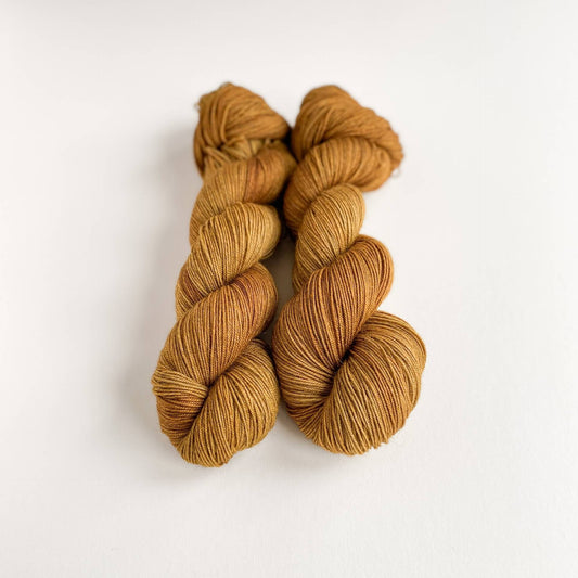 Two skeins of hand dyed yarn on a white table top. The yarn has been dyed with brown dyes on a yak base.