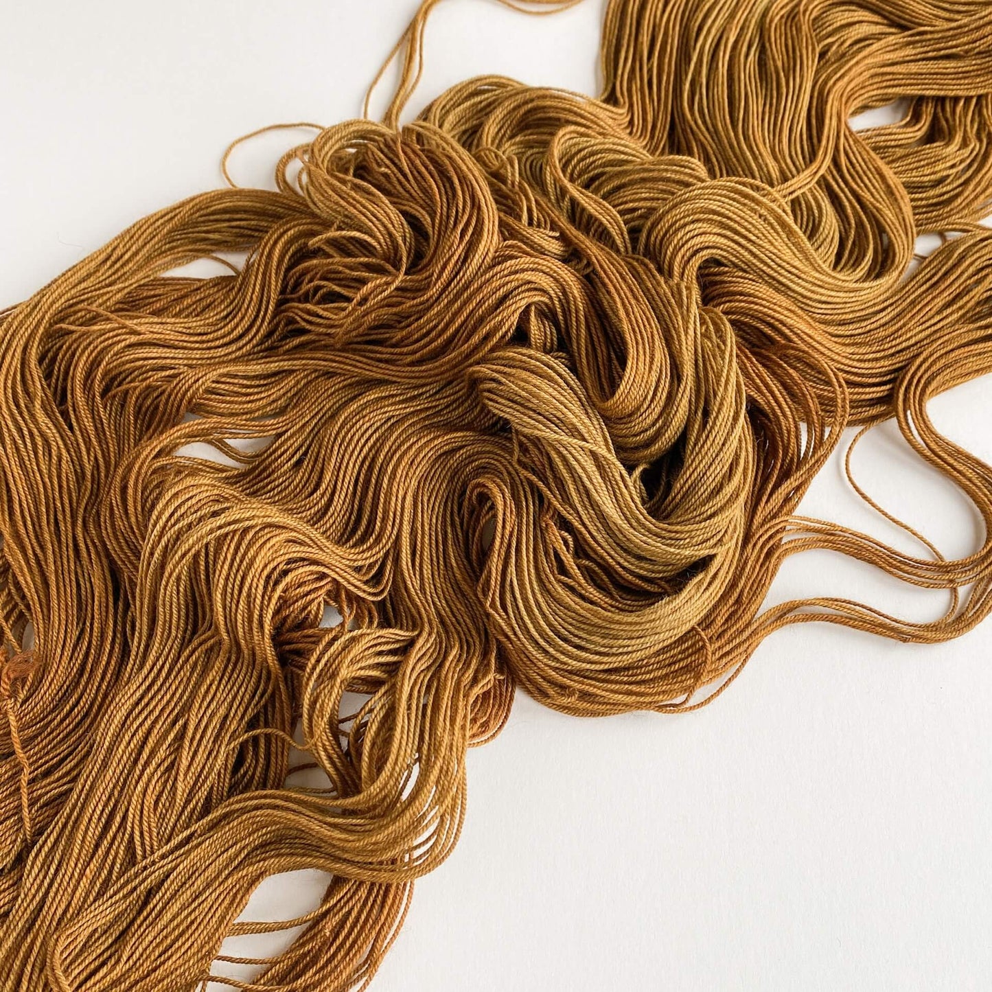 A rich brown skein of hand dyed yarn lies unfurled on a white table top.
