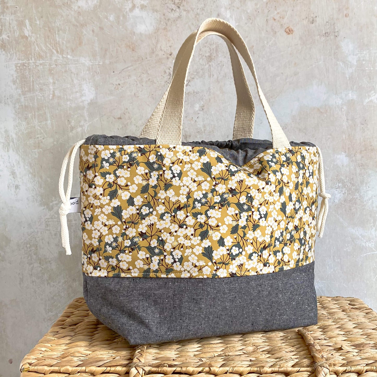 A side view of a large yellow floral knitting and crochet project bag. It has two sturdy handles and the bag base is a contrasting grey linen blend fabric. It is a good size for storing garment and blanket projects.
