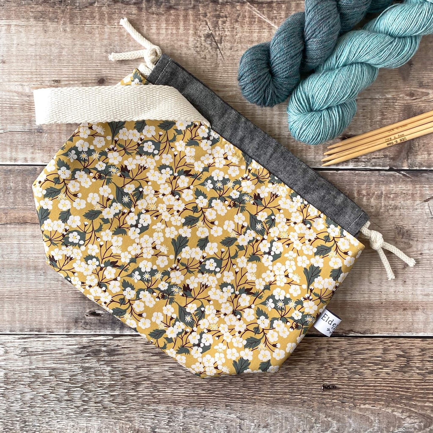 A flat lay of a yellow project bag designed for knitting and crochet projects. It is made from liberty of London floral fabric.