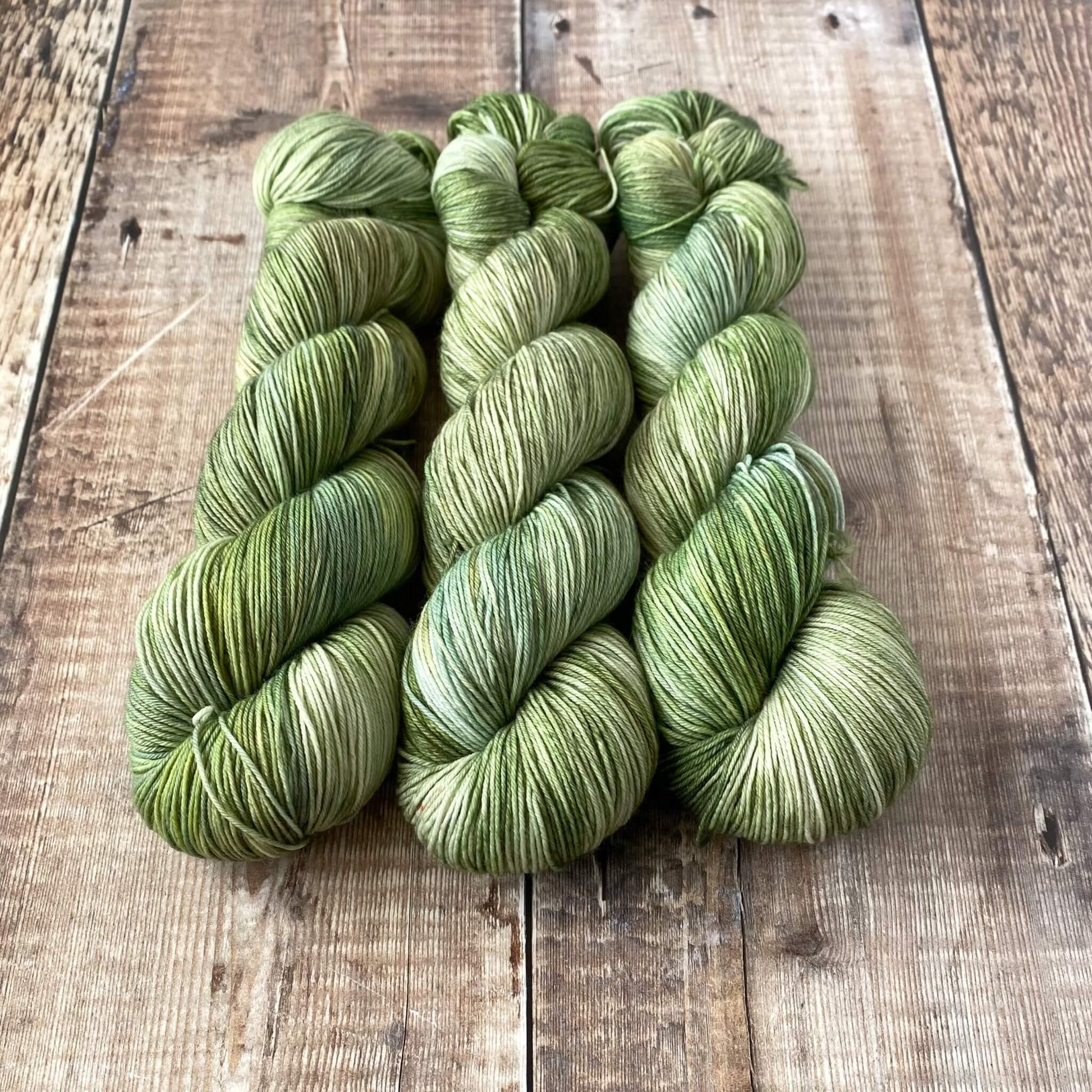 3 skeins of variegated yarn in greens and and greys, sitting on a wooden surface