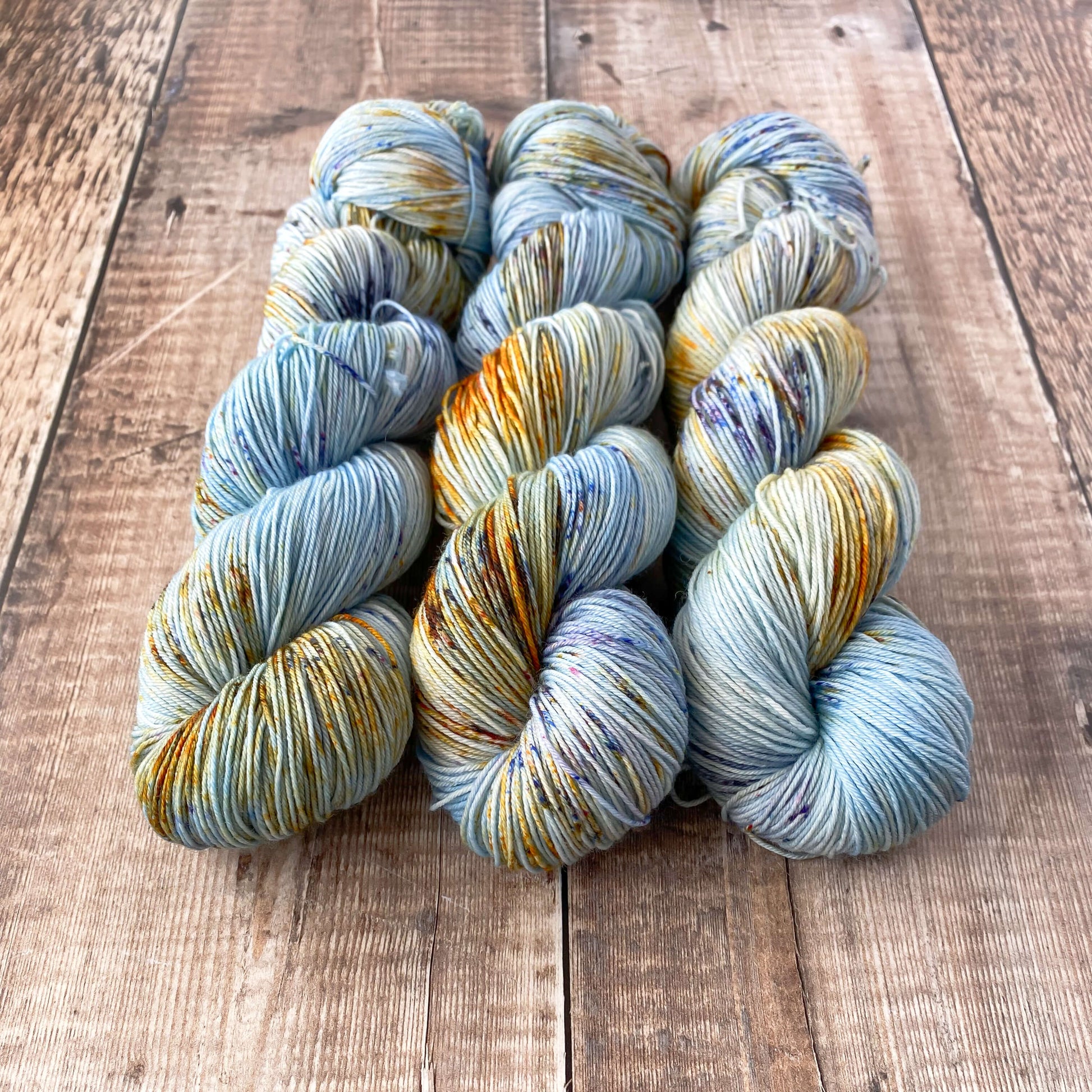 3 skeins of variegated yarn in blue, orange, brown, sitting on a wooden surface