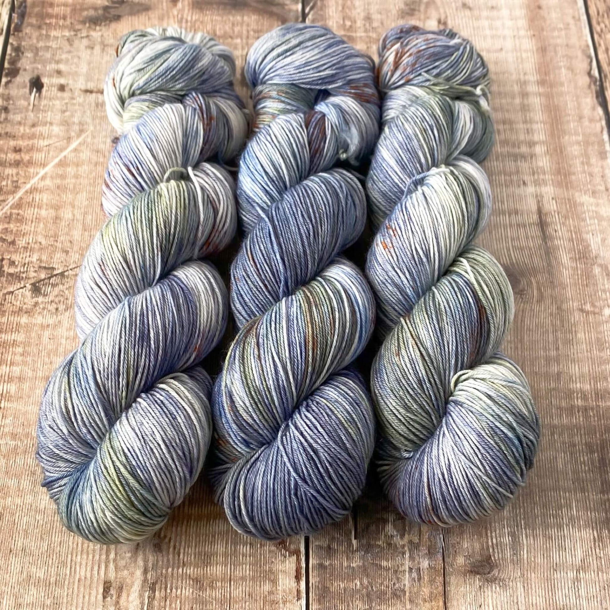 3 skeins of variegated yarn in blue, green, brown, sitting on a wooden surface