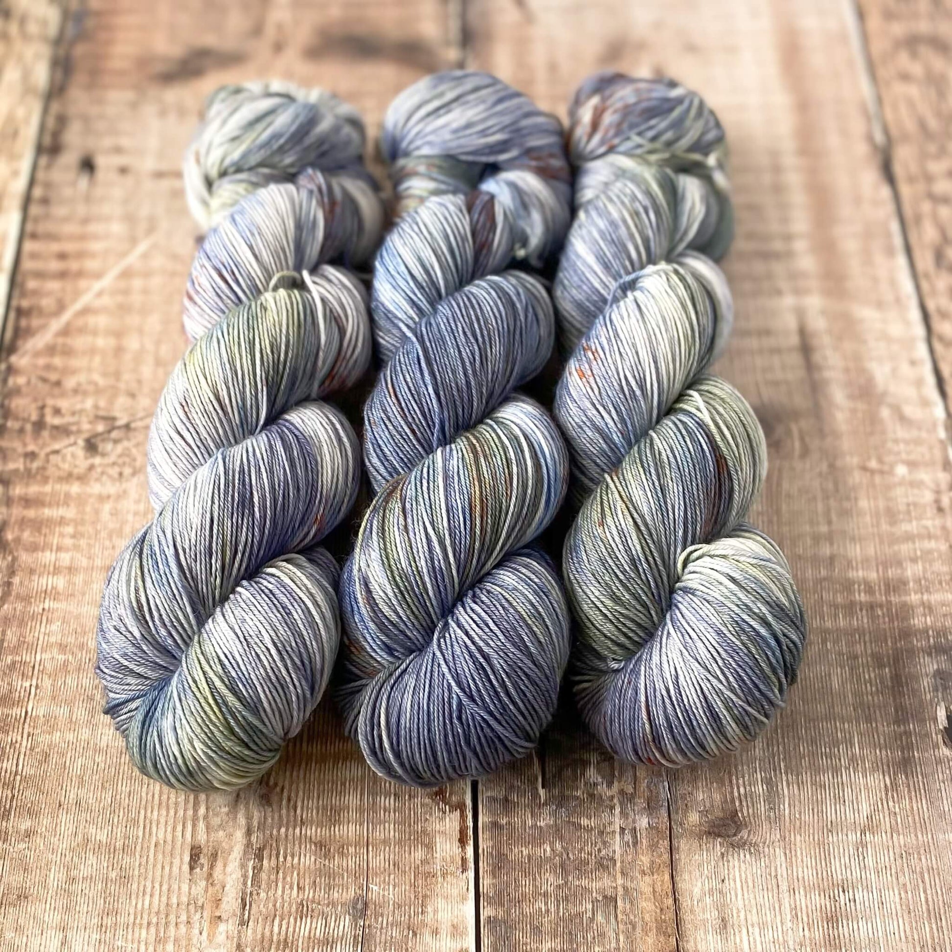 3 skeins of variegated yarn in blue, orange, brown, sitting in a line on a wooden surface