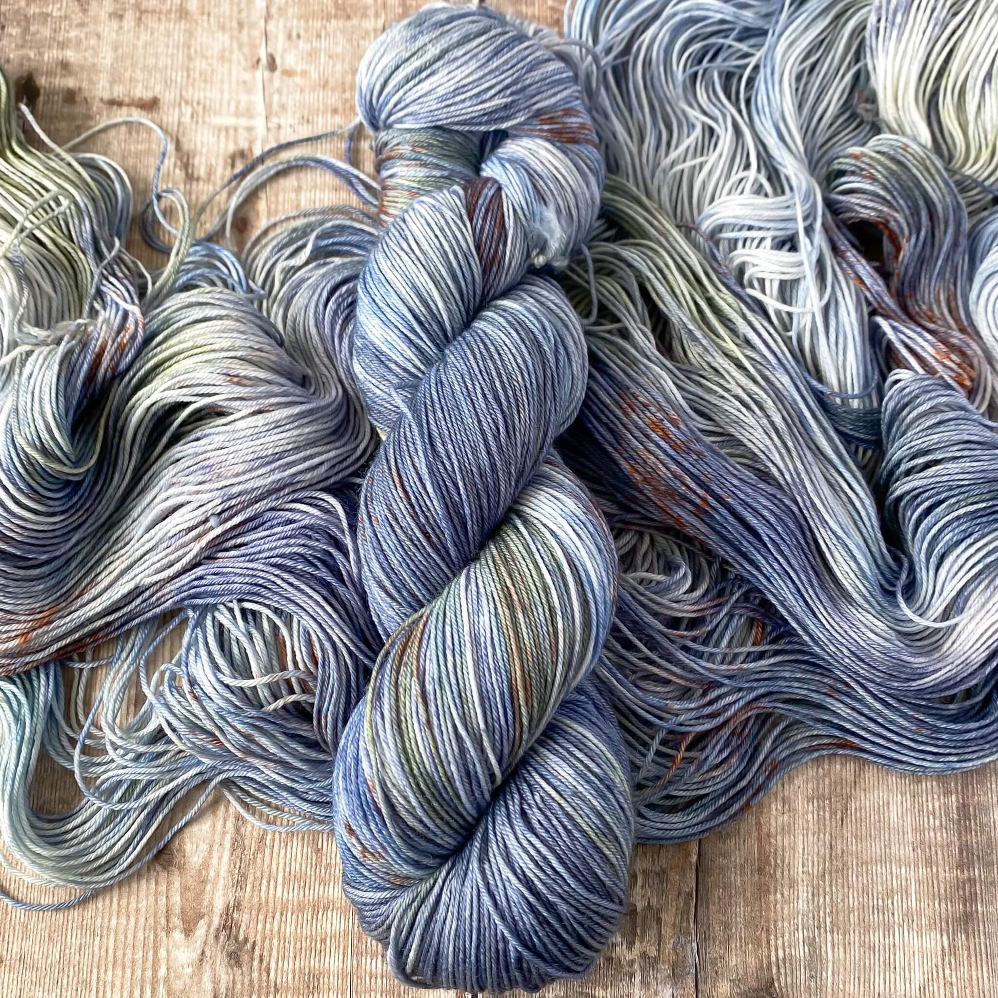 A skein of variegated yarn in blue, orange, brown, sitting on an unwound skein of yarn in the same colours.