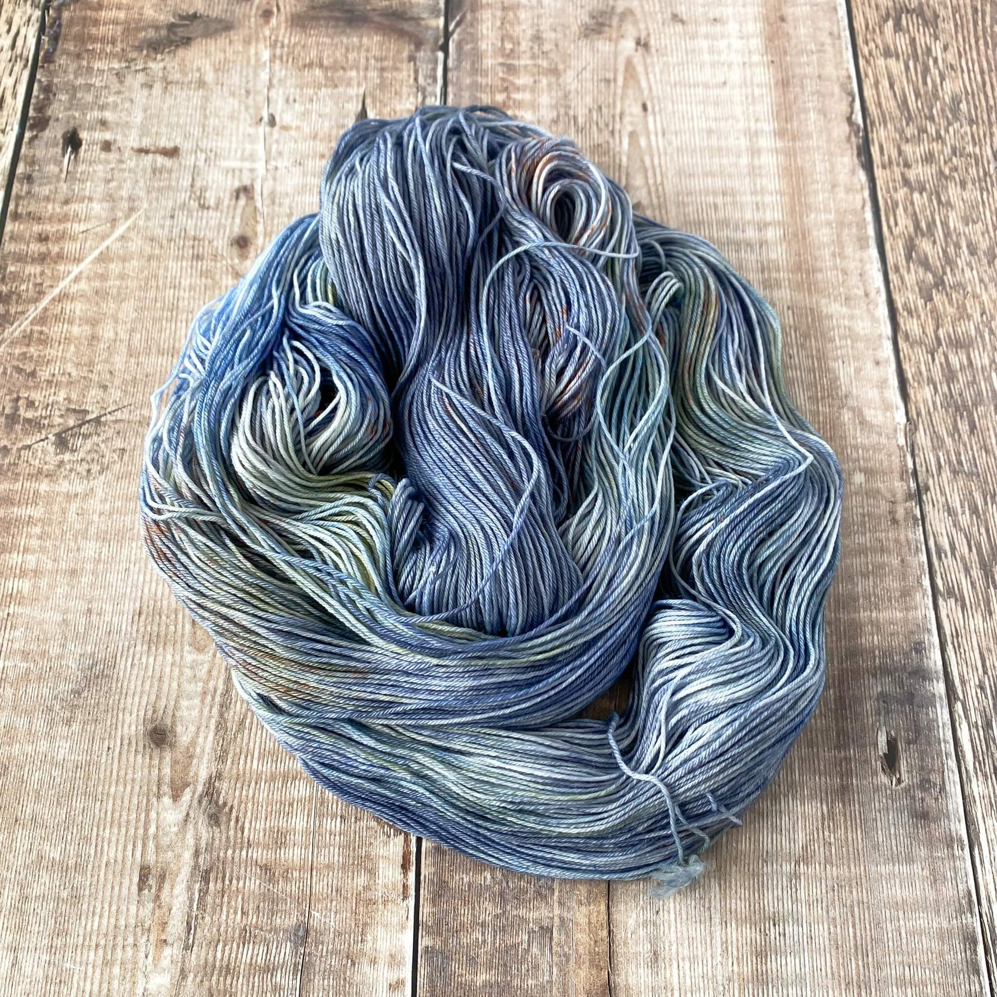 A coiled skein of yarn in blue, green and brown sitting on a wooden table