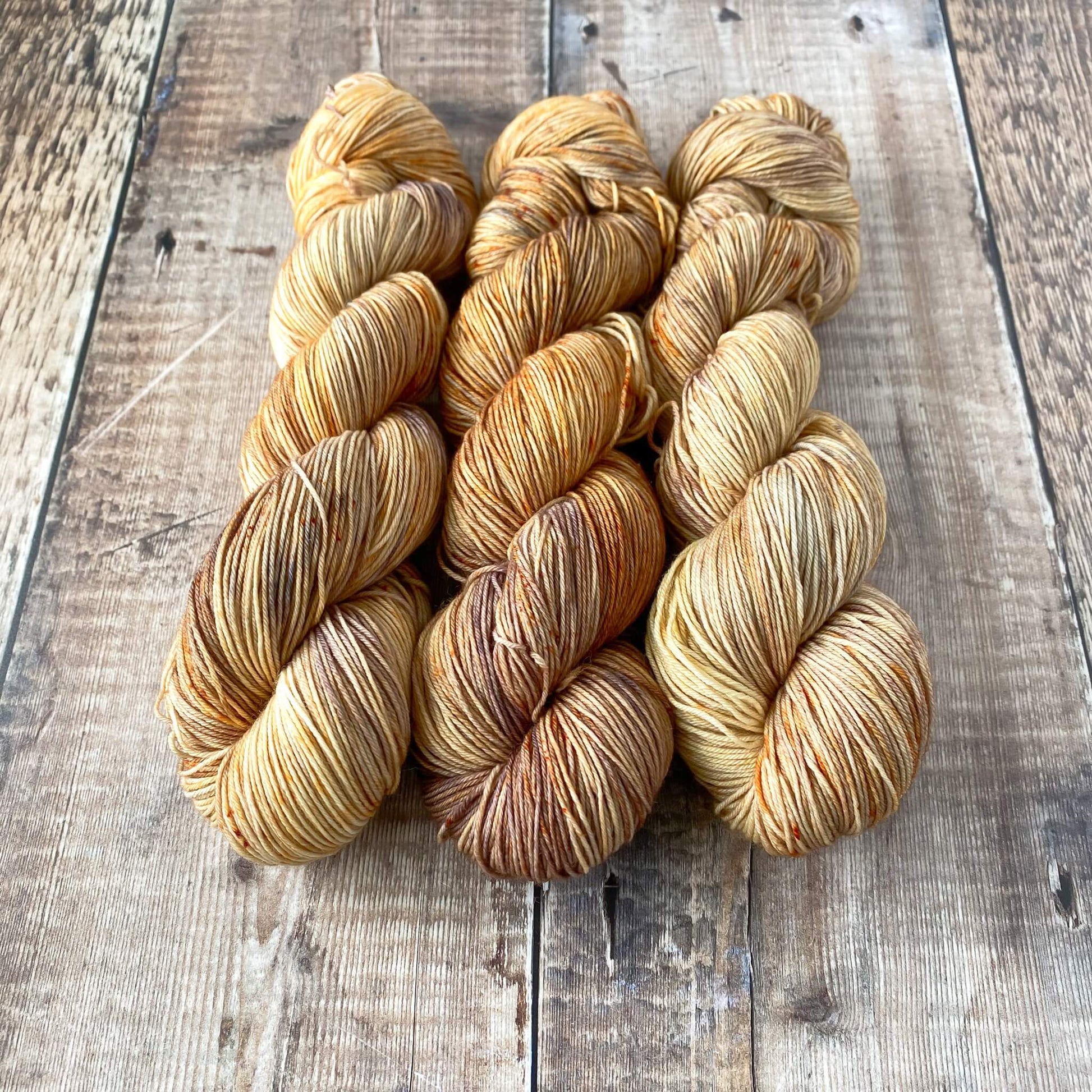 Three skeins of hand dyed yarn in browns and greys sitting on a wooden surface