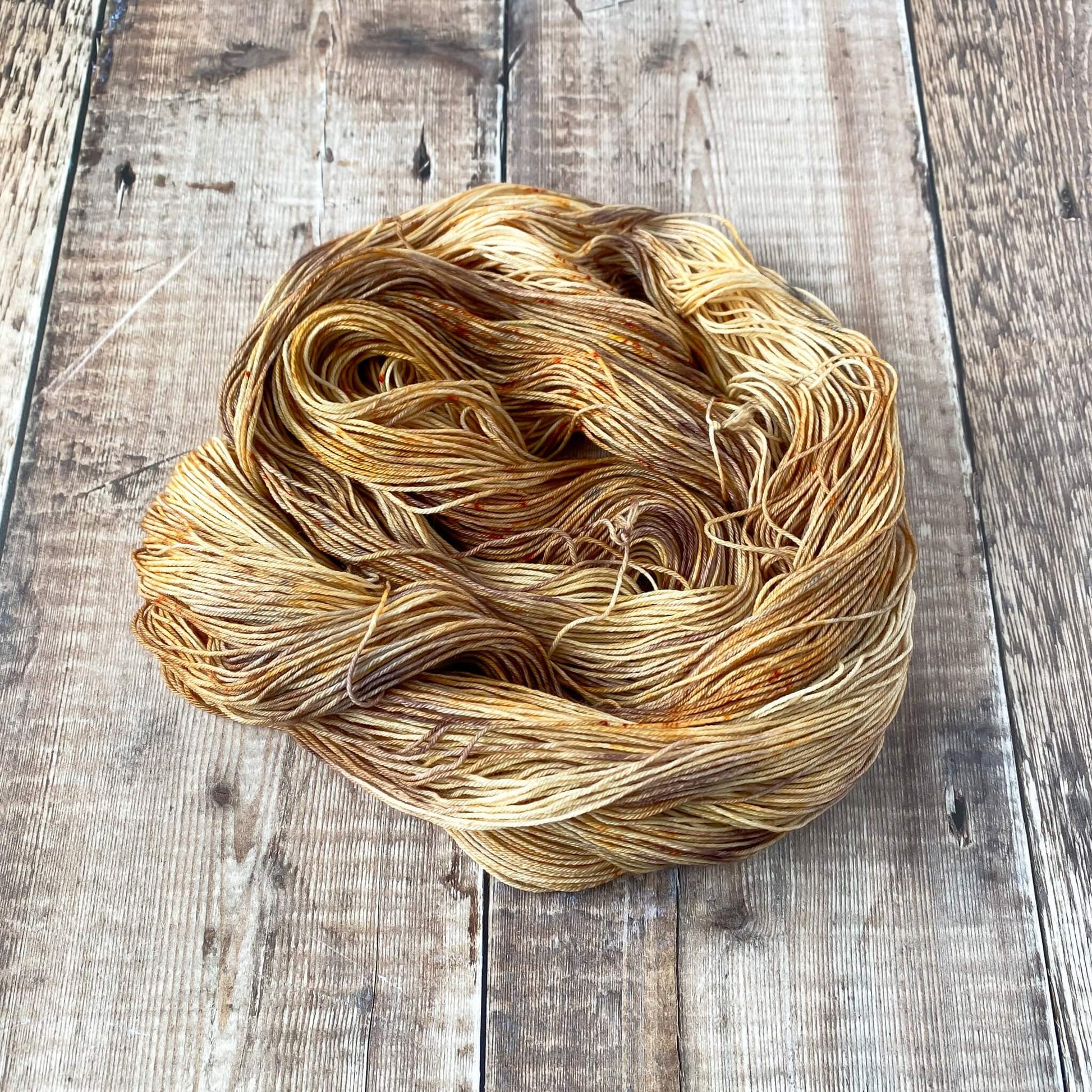 A skein of brown and grey hand dyed yarn sits in a coiled circle on a wooden surface