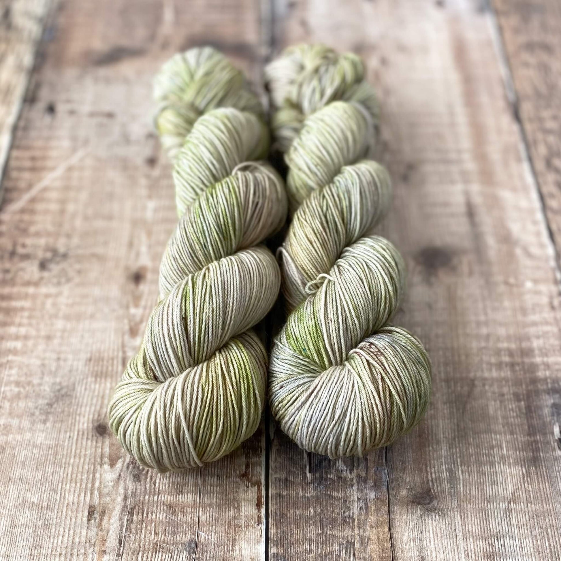 2 skeins of hand dyed yarn in green and grey on a wooden surface