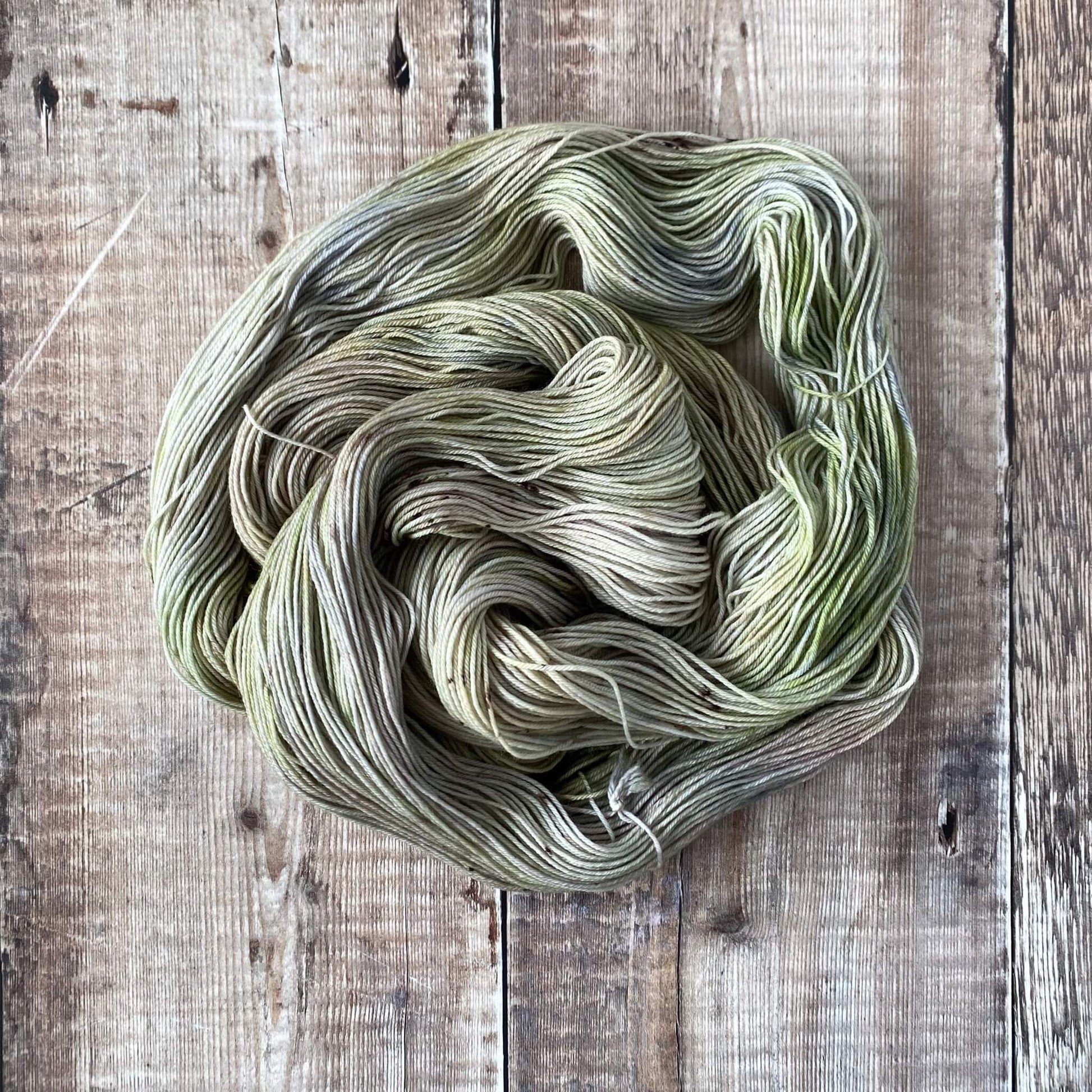 A skein of green and grey hand dyed yarn wound into a coil on a wooden surface