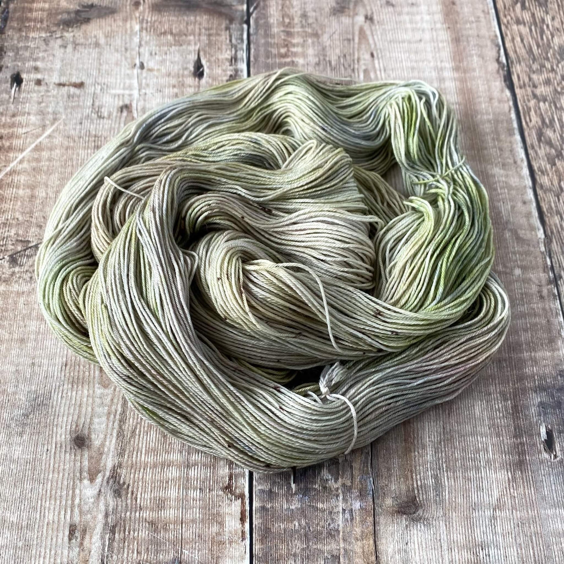 A coiled skein of hand dyed yarn coloured with green and grey dyes on a wooden surface
