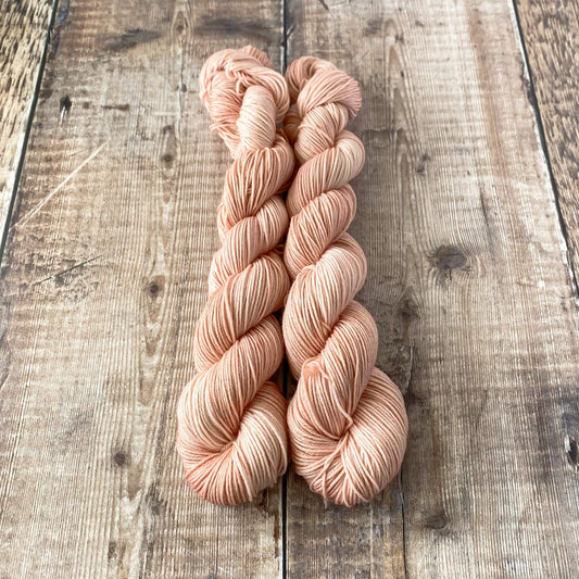 2 skeins of pink hand dyed yarn seen on a wooden surfact