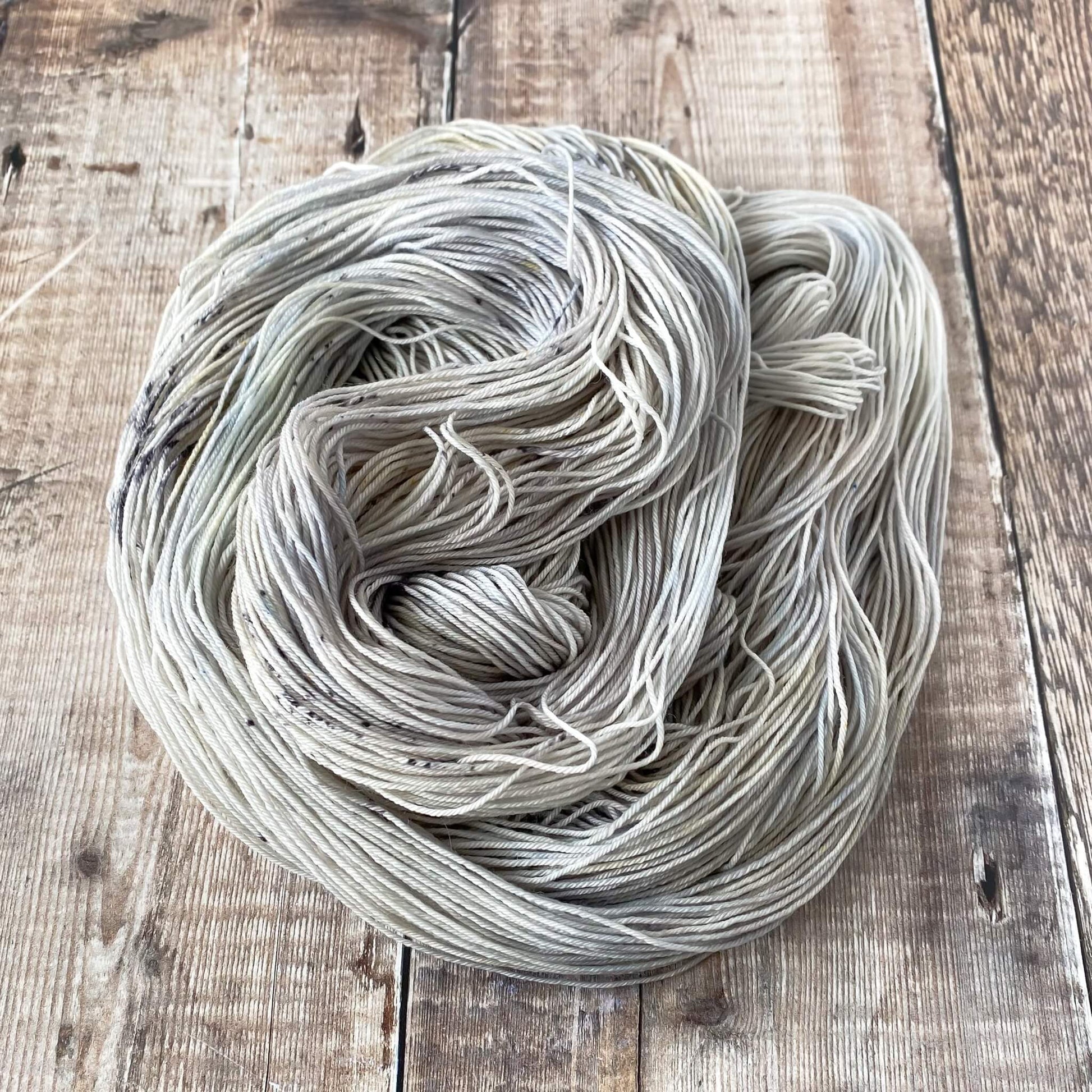 A pastel hand dyed skein of yarn coiled in a circle and sitting on a wooden surface.