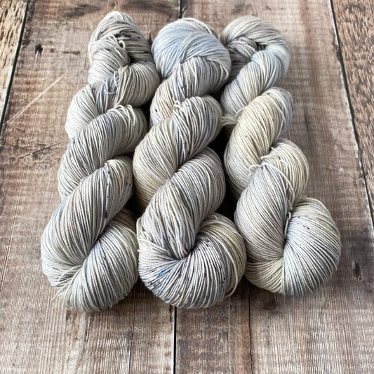 Three skeins of pastel hand dyed yarn in blues, greys and browns on a wooden surface