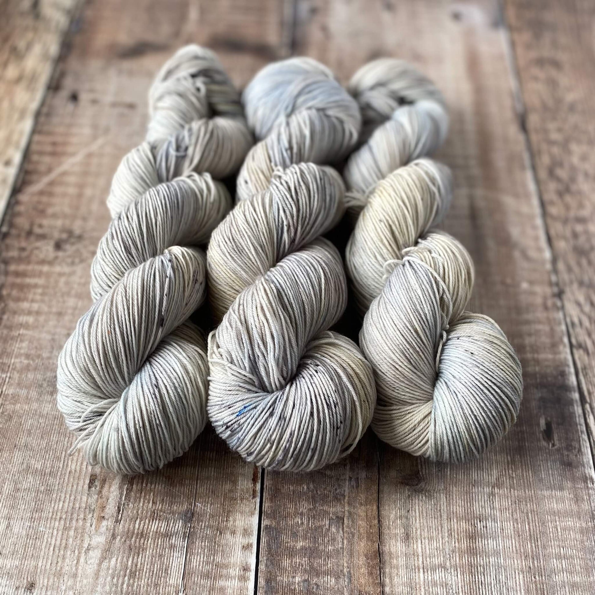 Three hand dyed skeins of yarn on a wooden surface. Coloured in blues, greys and browns.