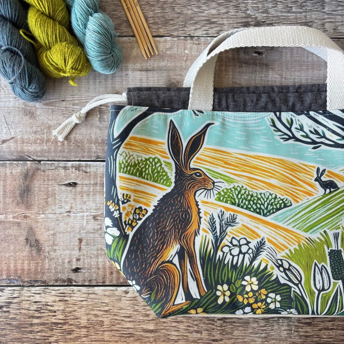 Fabric bag with animal design on a wooden surface with yarn and knitting needles.