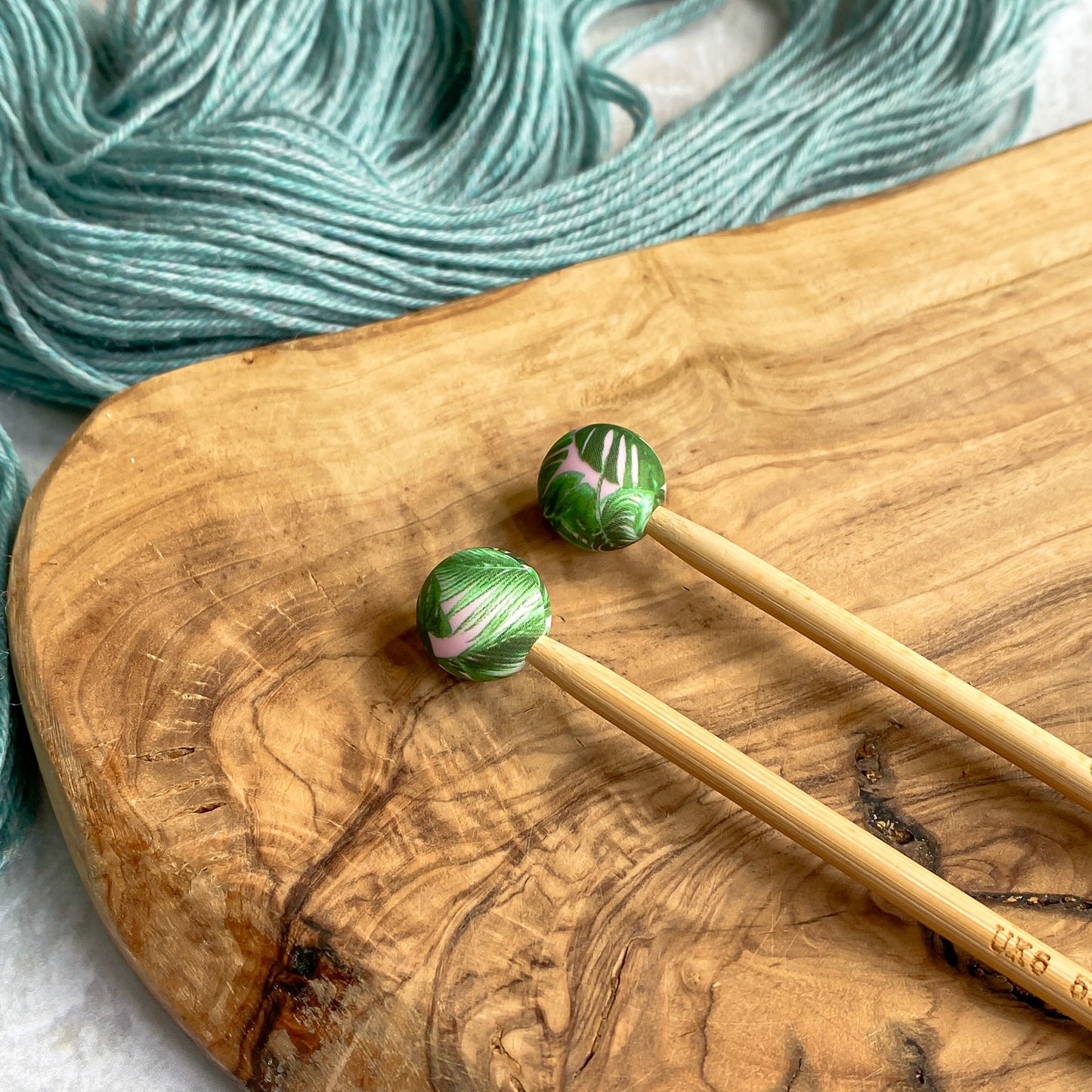 Two silicone needle protectors attached to knitting needles to stop stitches falling off. The needle protectors are designed in a palm leaf print.
