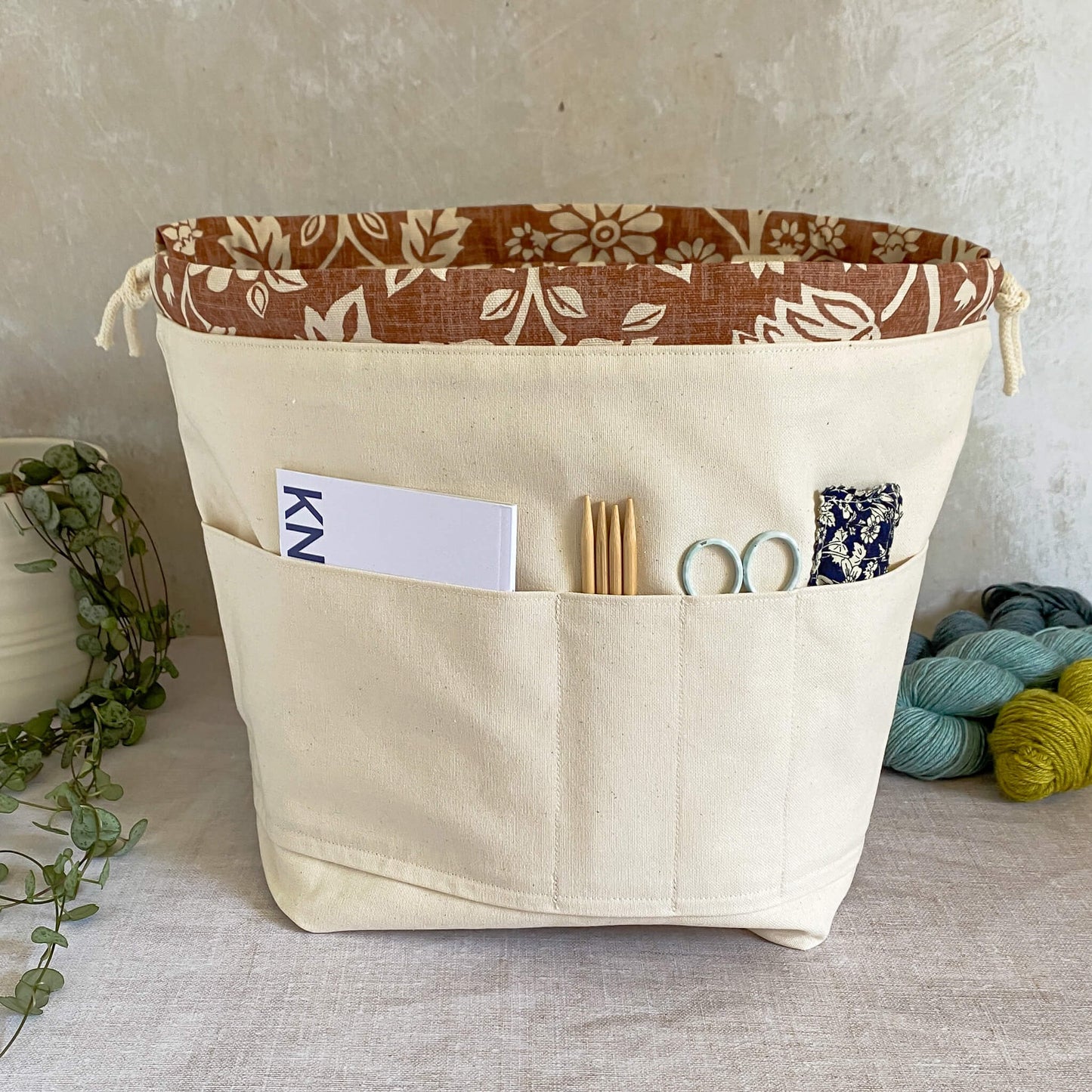 The inside of a large knitting and crochet project bag showing the pockets on one side of the bag. The pockets can be used to hold a knitting or crochet pattern, a notebook, pen, knitting needles and crochet hook and other crafting accessories. The interior of the bag is made from a sturdy natural coloured canvas.