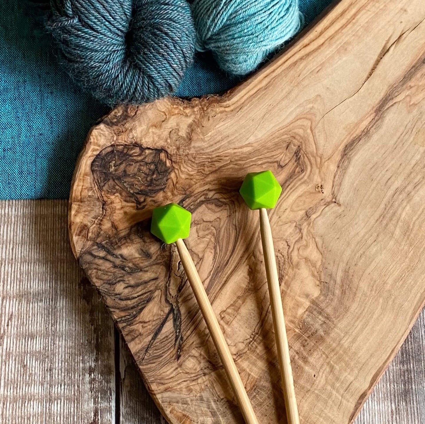Chartreuse needle protectors to stop stitches escaping from knitting needles. A pair sit on a wooden table attached to knitting needles.
