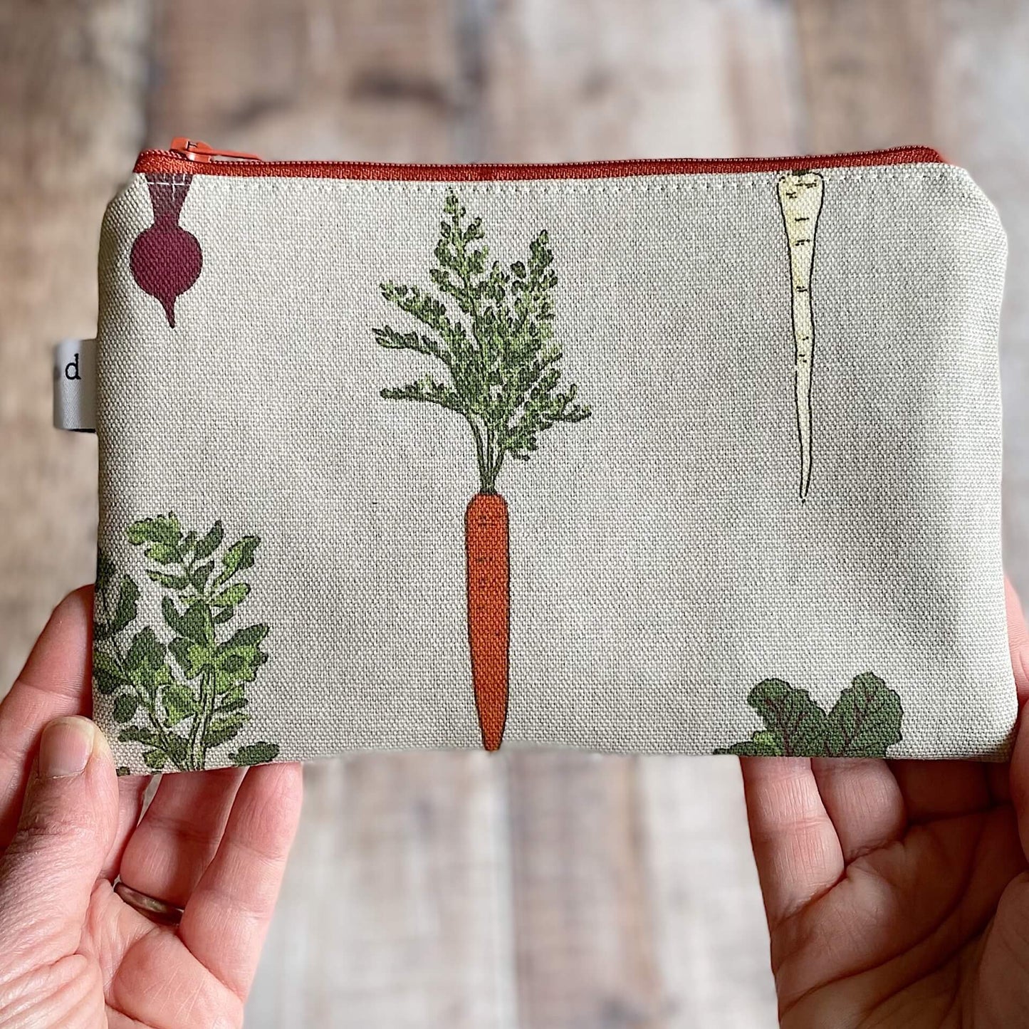 A knitting notions pouch, hand made by Eldenwood Craft, is held up in front of a wooden table.