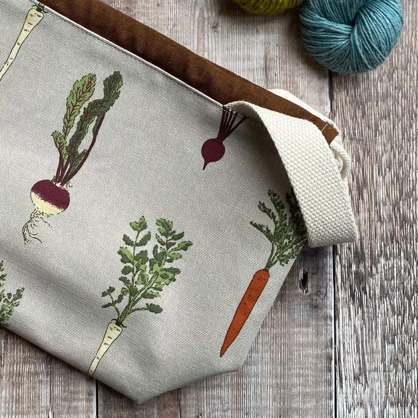 A handmade project bag lies on a table next to two skeins of yarn.