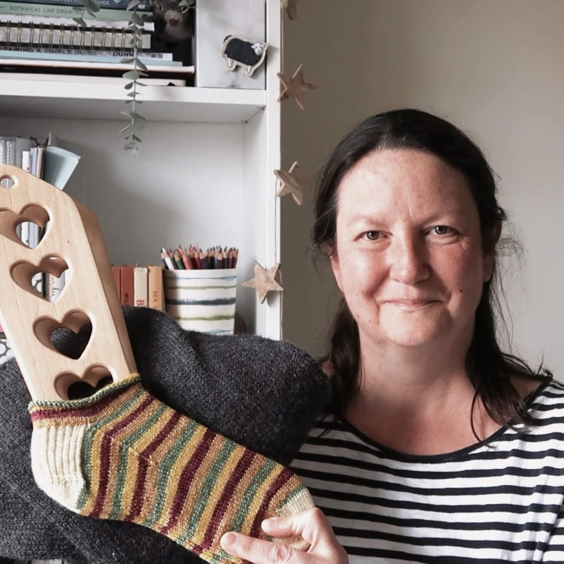 Eldenwood Craft Knitting podcast - Emma holds up a pair of socks and a sweater to the camera as she records