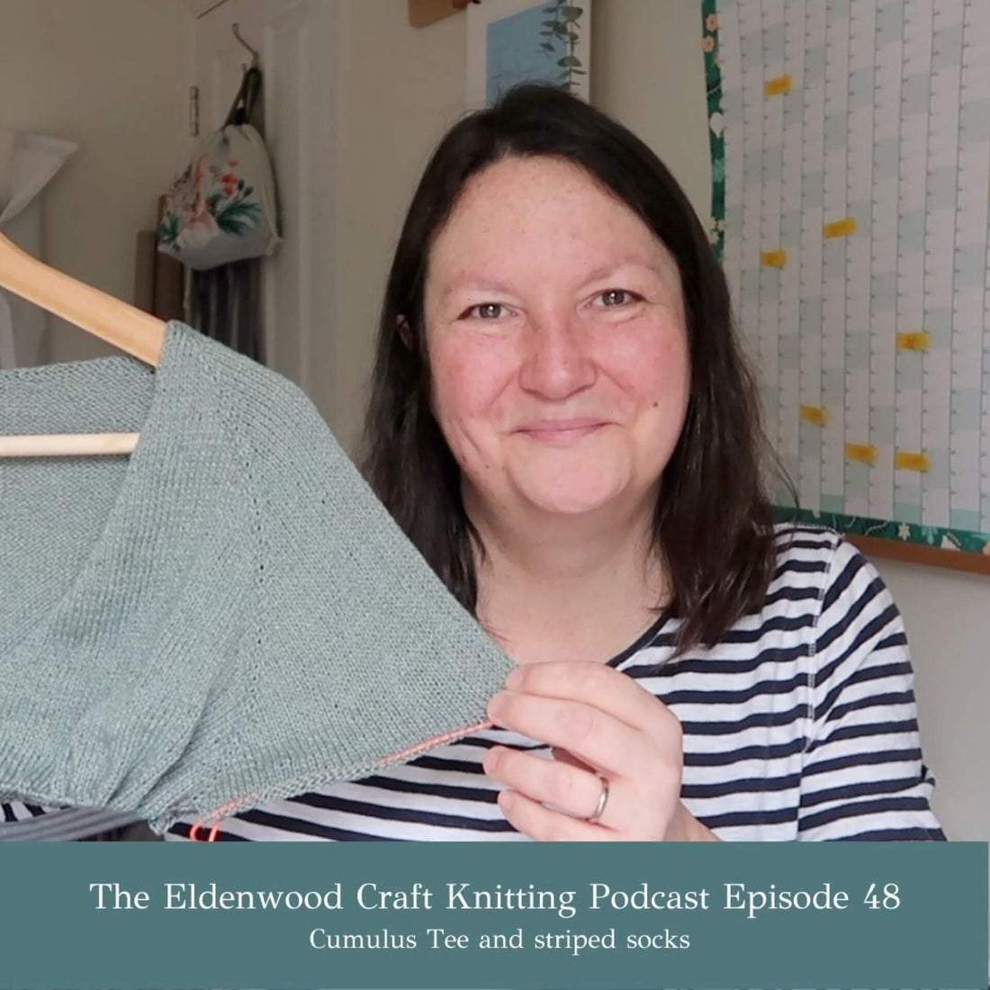 Emma, the presenter of the Eldenwood Craft Knitting Podcast on YouTube, shows off her partially knitted Cumulus Tee. She is wearing a blue and white striped top.