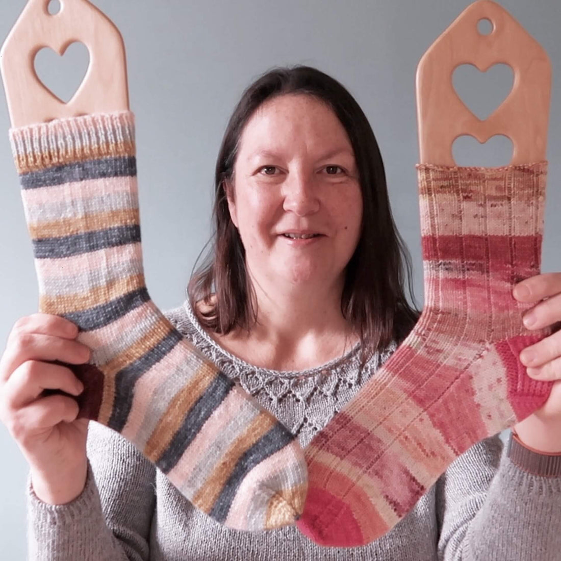 Emma, the host of the Eldenwood Craft podcast, shows two finished handknit socks she's been working on. Both are striped - one is blue based and the other is very pink!