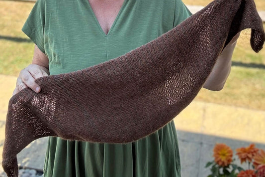 A knitter holds up a brown small scarf which is a featured item in a knitting podcast