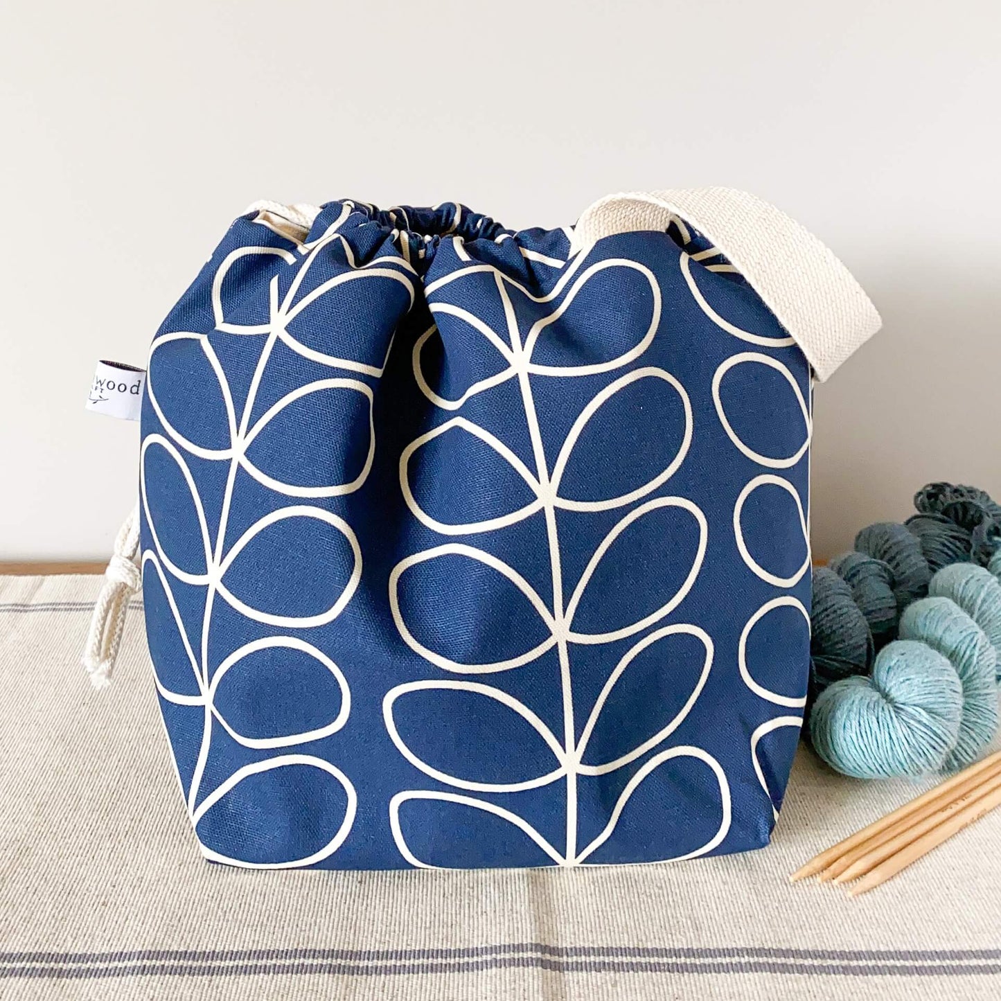 A navy blue knitting project featuring a linear stem print sits on a table next to two skeins of blue yarn and a set of wooden knitting needles. 