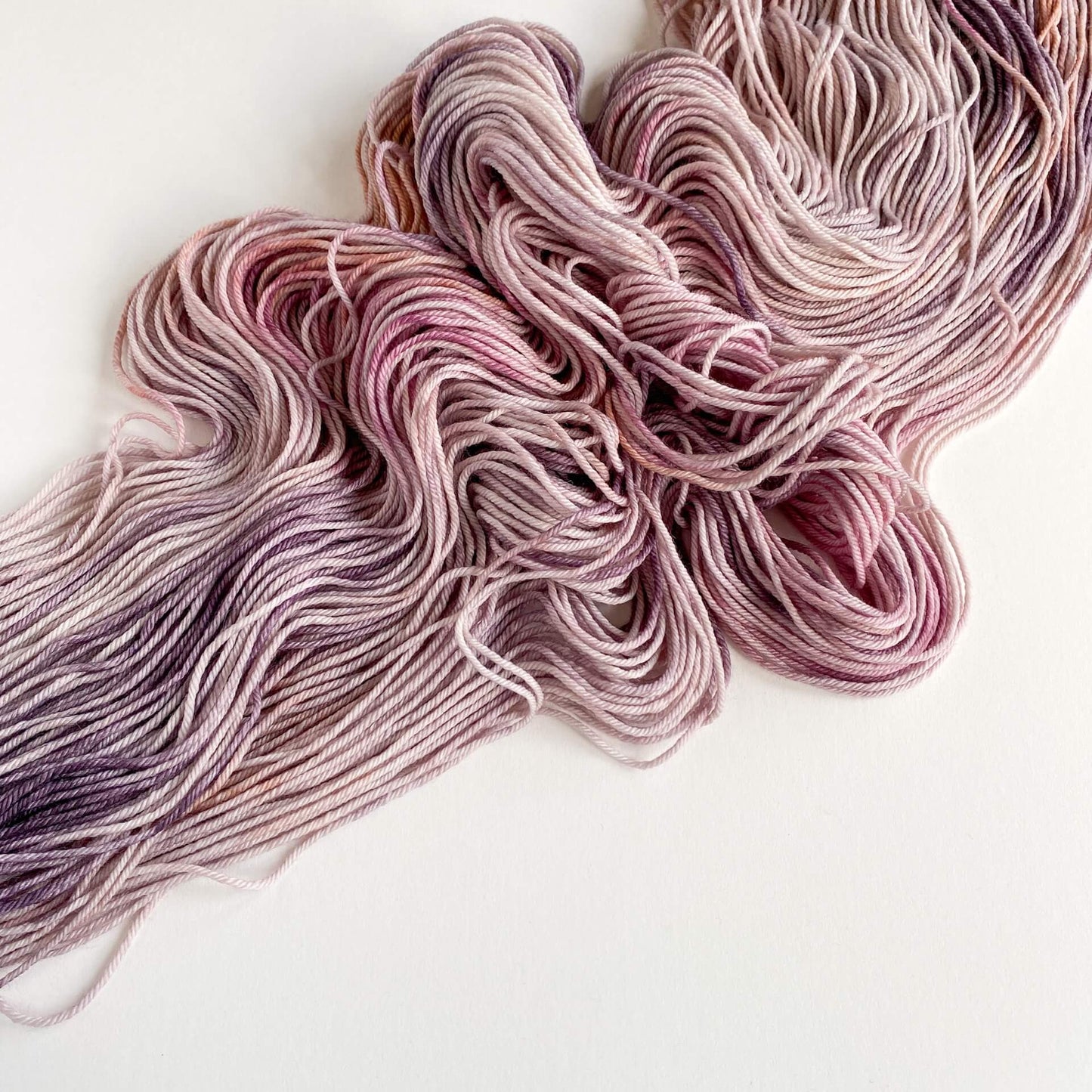 A skein of yarn lies unwound on a white background. They yarn is coloured with pinks and purples. 