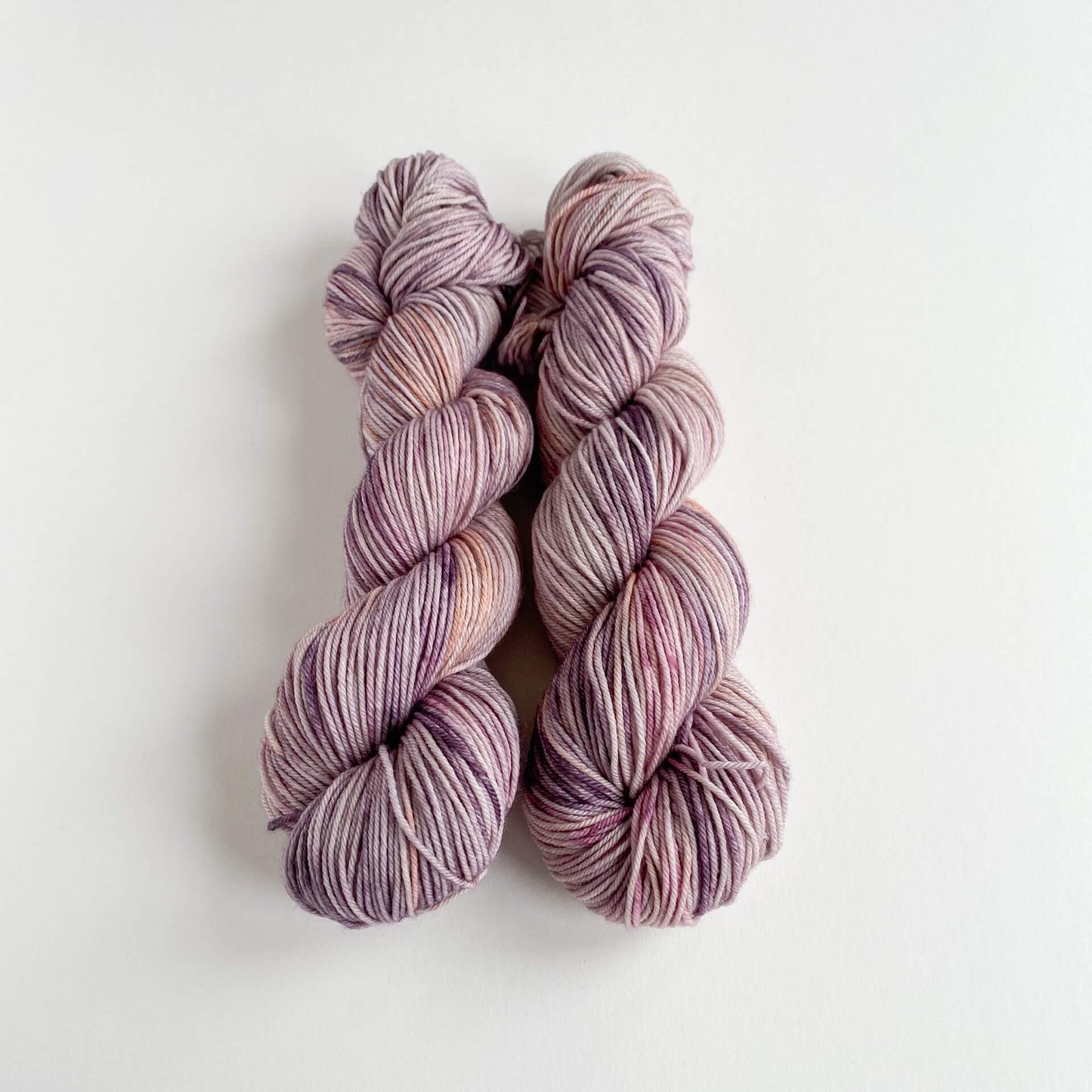 Two skeins of yarn lie wound up on a white background. They are coloured with pink and purple dyes.