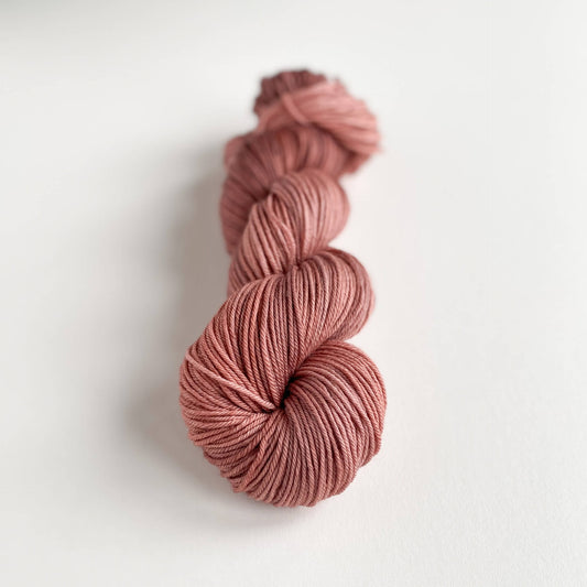 A skein of yarn lies wound up on a white background. The yarn is coloured a deep pink colour. 