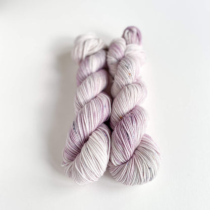 Two skeins of hand dyed yarn on a white table top. The yarn has been dyed with purple and grey dyes. 