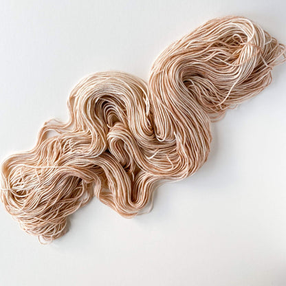 A pink coloured hand dyed yarn has been unfurled from its skein and tossed onto a white table top