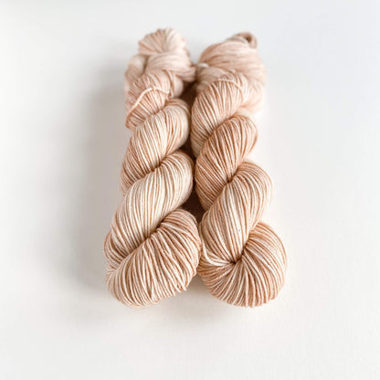 Two skeins of hand dyed yarn on a white table top. The yarn has been dyed with brown and pink dyes. 