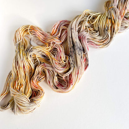 Unfurled yarn has been thrown across a white board. The yarn is coloured with black and red and yellow dyes. 