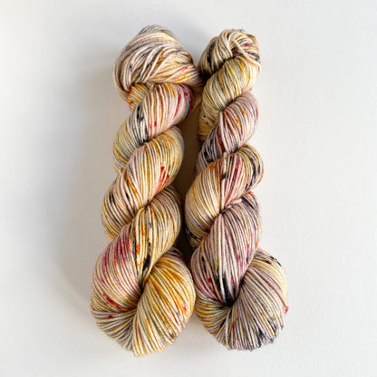 Two skeins of yarn sitting on a white background. The yarn has been dyed with yellow and black and red dyes, bringing out some of the colours found in a puffin