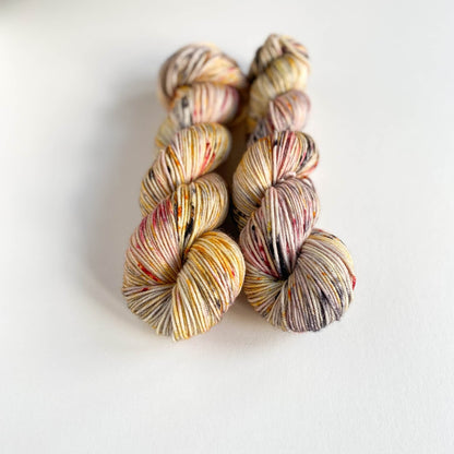 Two skeins of yarn sitting on a white background. The yarn has been dyed with yellow and black and red dyes, bringing out some of the colours found in a puffin